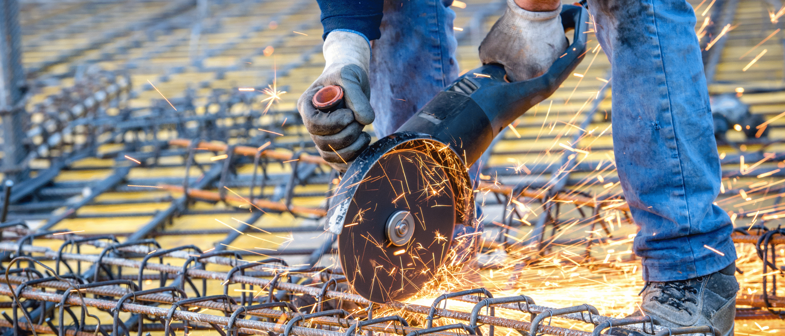 Construction worker using an angle grinder to cut steel rebar with sparks flying at a job site, illustrating factors that can impact overall construction permit cost.